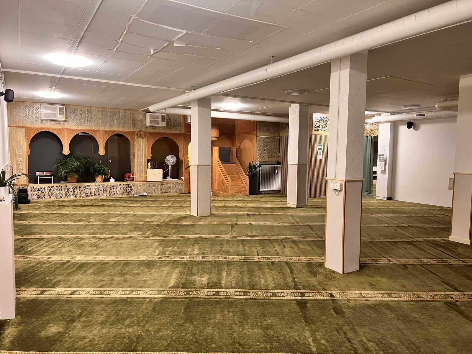 Der Hauptgebetsraum der Moschee: heller Raum, grüner Teppich, geschnitzte Holzbögen.