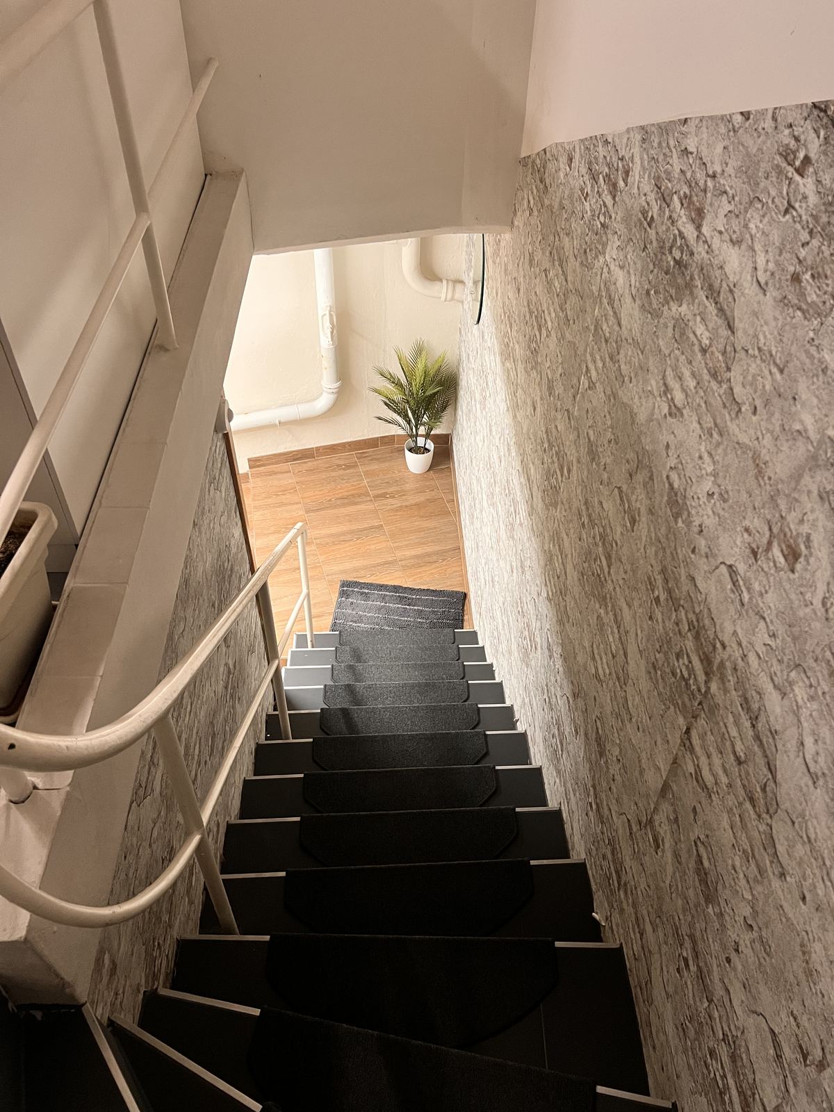 Treppe mit dunklen Stufen und weissem Handlauf, die zwischen einer Steinwand hinunterführt.